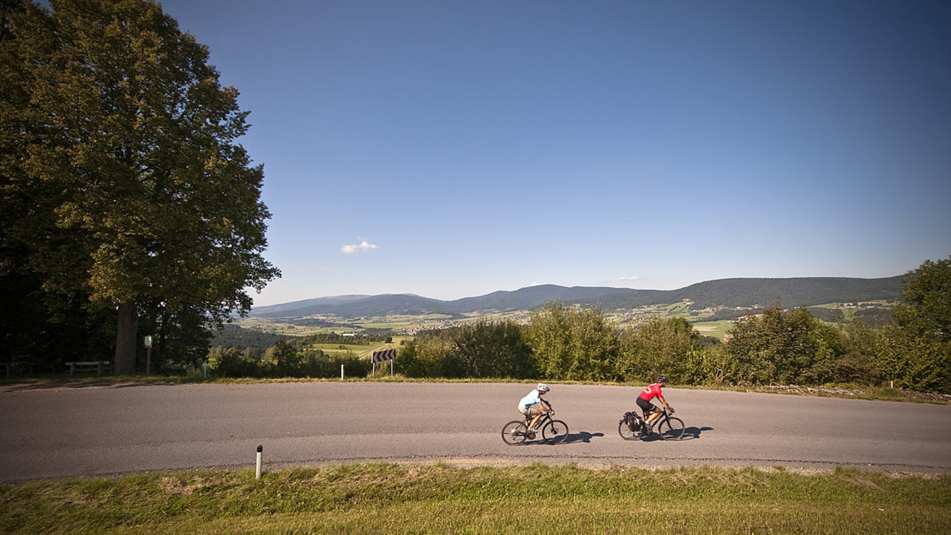 Foto: Oberösterreich Tourismus GmbH/Erber: Radfahren am Mühlviertelradweg R5 Hier sieht man zwei Radfahrer, die entlang einer asphaltierten Straße dem Mühlviertelradweg befahren.